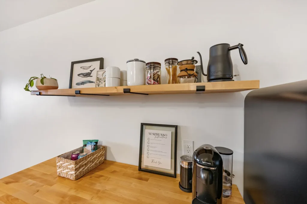 Modern kitchen coffee station with wooden shelf.