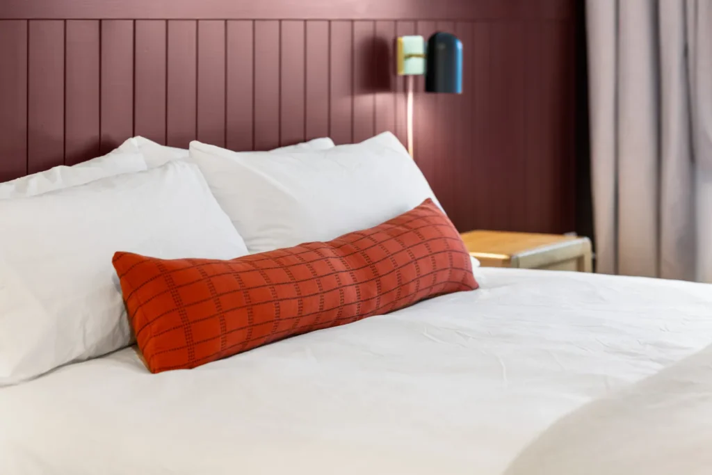 Cozy bed with red pillow and white linens